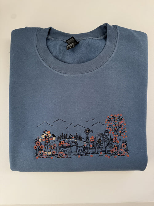 Autumn Farm line art embroidered on an Indigo Blue crewneck: scarecrow, pickup truck, windmill, barn and orange pumpkins