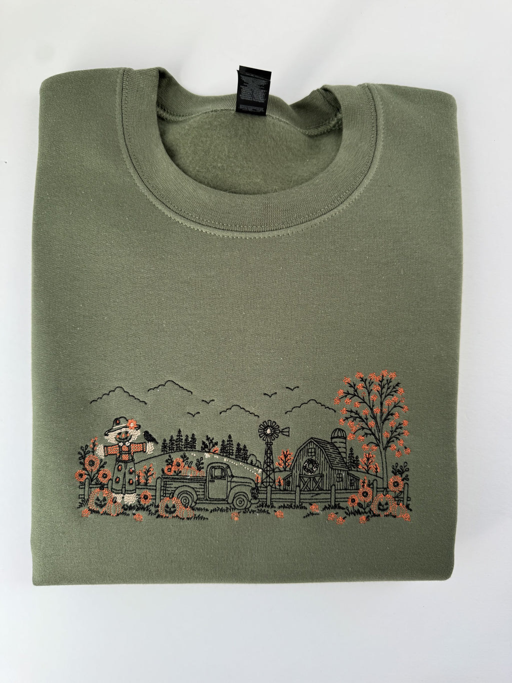 Autumn Farm line art embroidered on a Military Green crewneck: scarecrow, pickup truck, windmill, barn and orange pumpkins