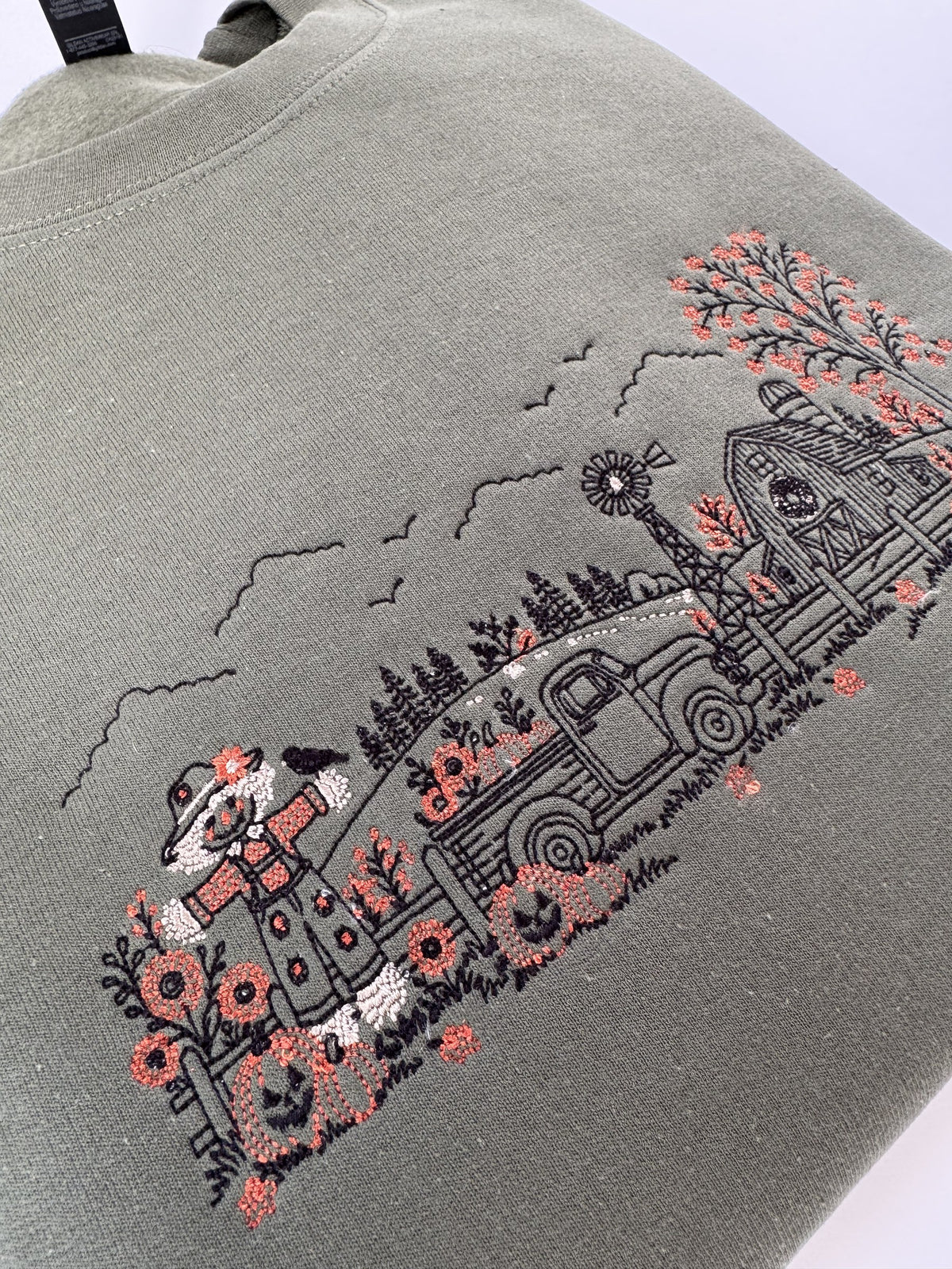 Close up of the scarecrow, jack-o-lanterns and pickup truck on the Military Green Autumn Farm crewneck