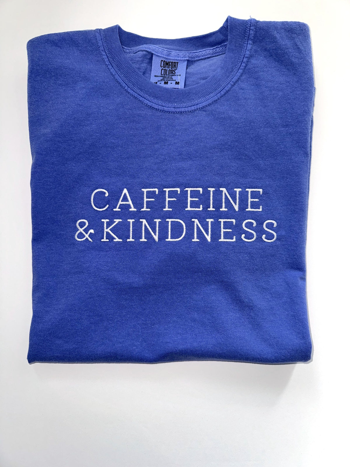 Caffeine and Kindness embroidered in white thread on a Flo Blue tee