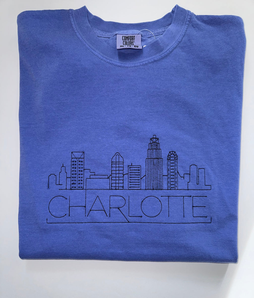 Charlotte skyline and CHARLOTTE embroidered in black thread on a Flo Blue tee