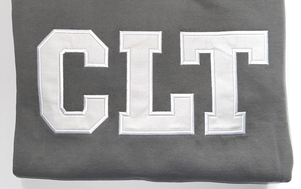 Close up of the white CLT appliqué letters on a Pepper crewneck