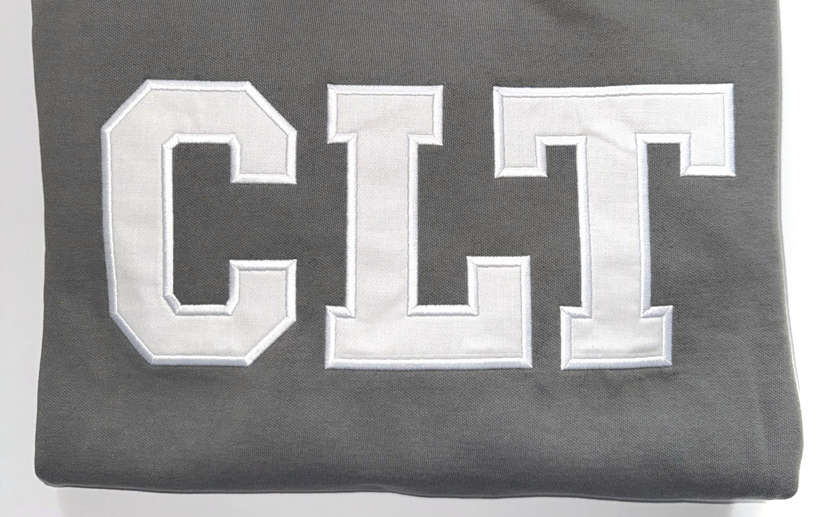 Close up of the white CLT appliqué letters on a Pepper crewneck