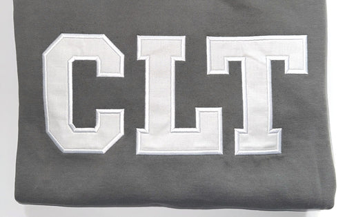 Close up of the white CLT appliqué letters on a Pepper crewneck