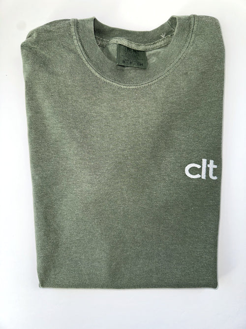 Small white clt embroidery on the chest of a folded Moss tee