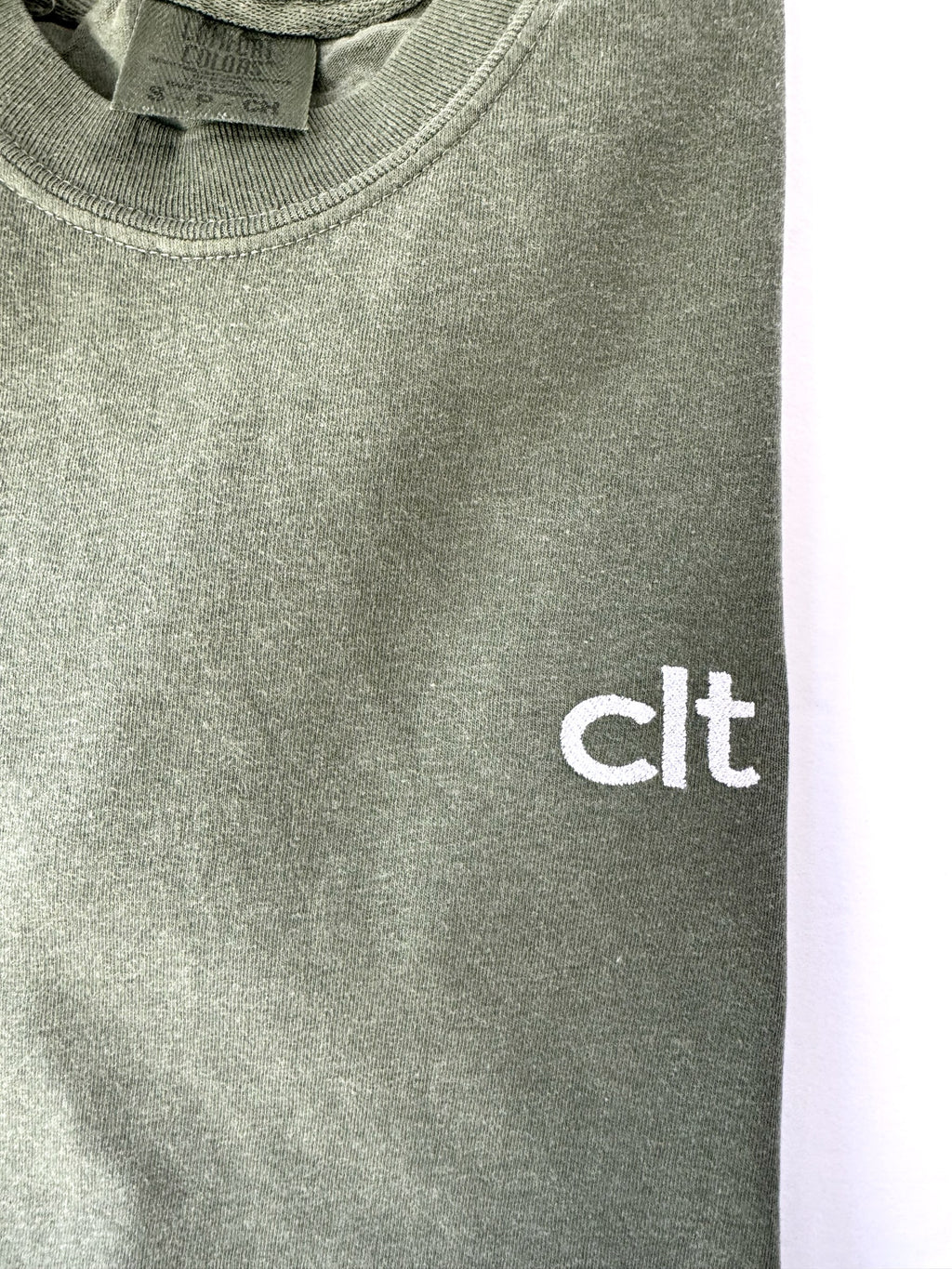 Close up of the white clt embroidery on a Moss tee