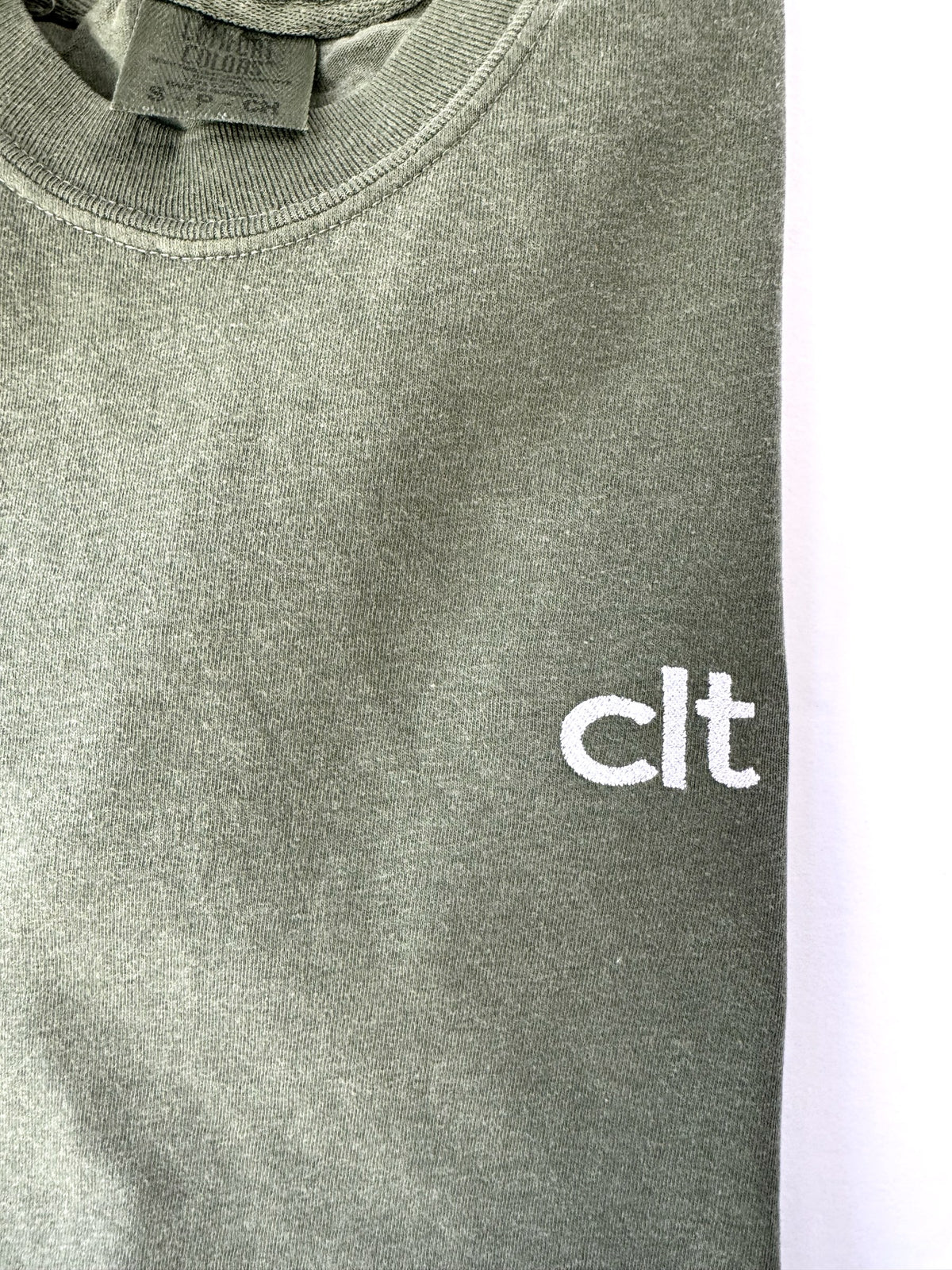 Close up of the white clt embroidery on a Moss tee