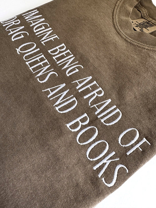 Close-up of the cream embroidered lettering on the "Imagine being afraid of drag queens and books" tee in Espresso