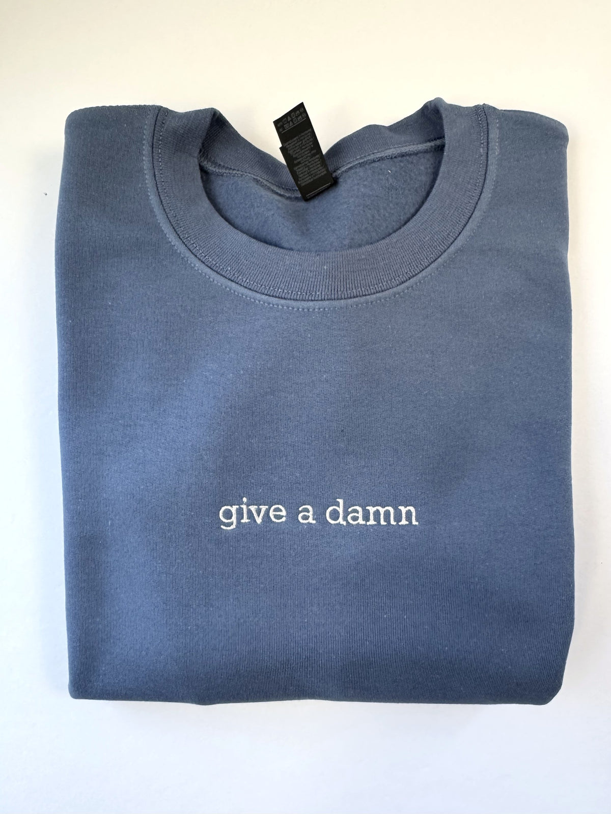 Give a Damn embroidered in white thread on an Indigo Blue crewneck
