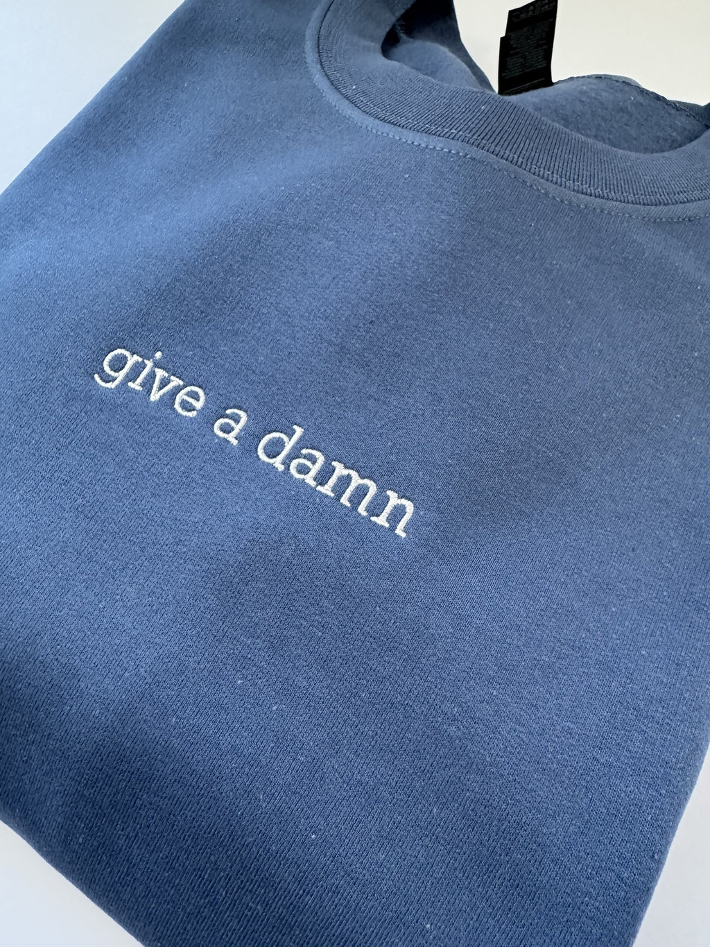 Close up of the Give a Damn embroidery on an Indigo Blue crewneck