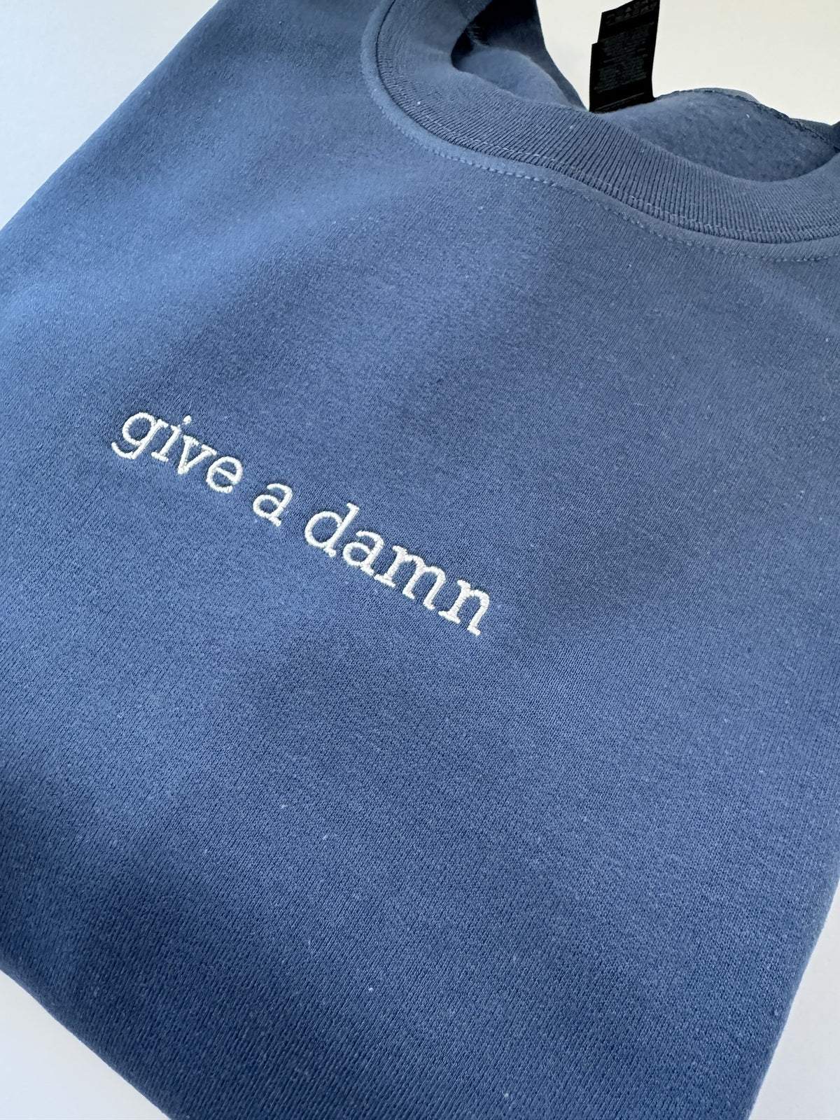 Close up of the Give a Damn embroidery on an Indigo Blue crewneck