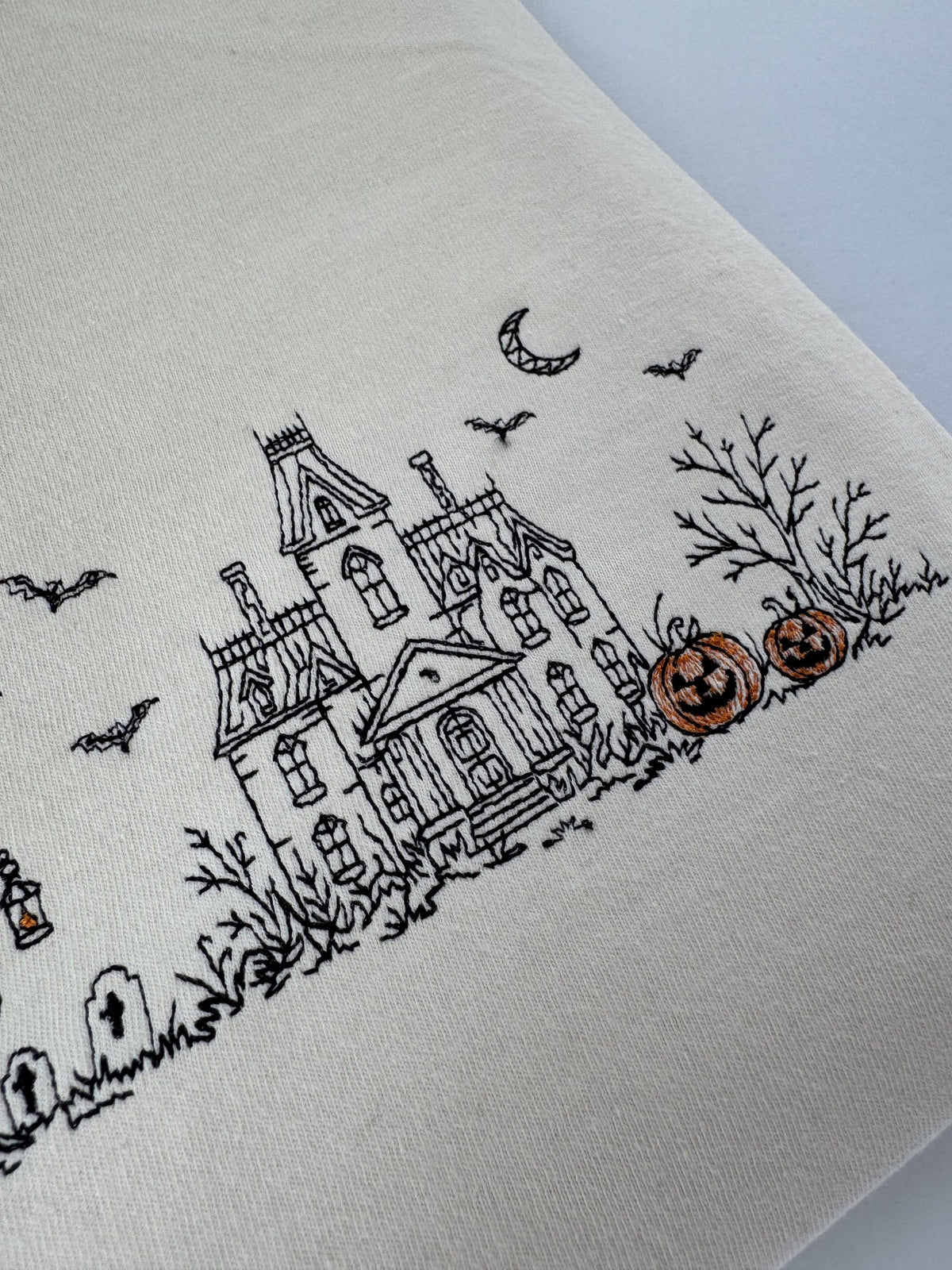 Close up of the witch reading on a stump, the graveyard and the ghost with a lantern in the Haunted Manor embroidery