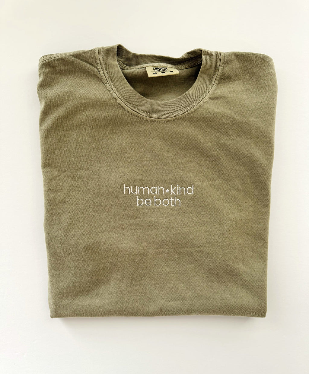 human kind be both embroidered in white thread on a Khaki tee