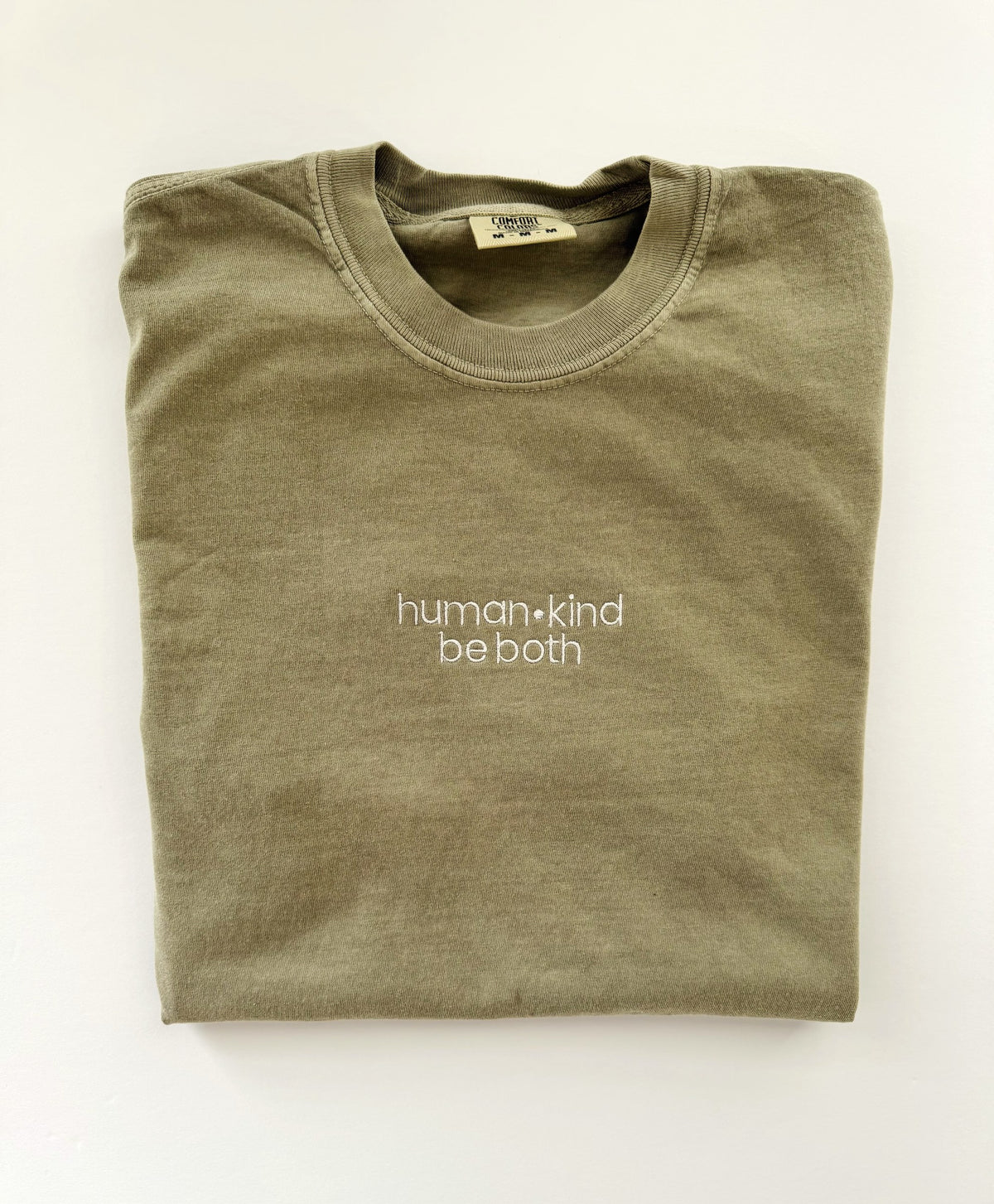 human kind be both embroidered in white thread on a Khaki tee