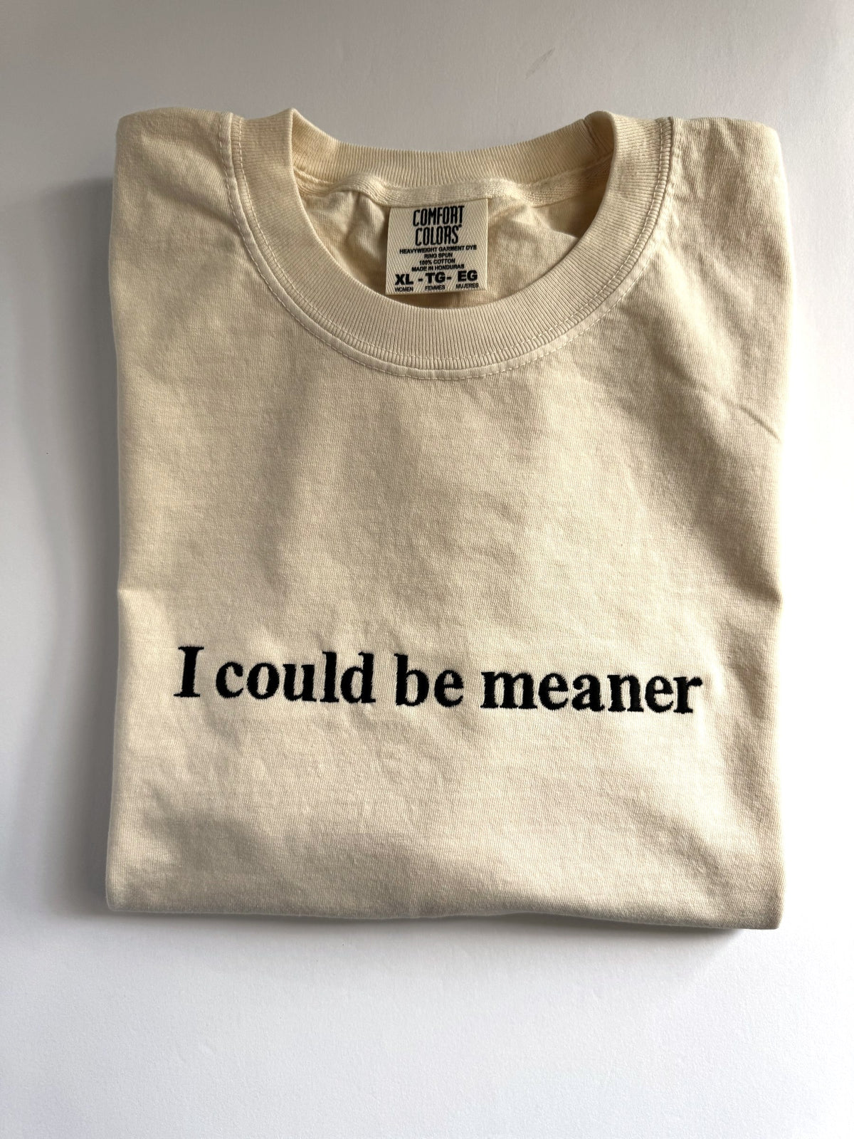 "I could be meaner" embroidered tee in Ivory, folded flat with the collar showing