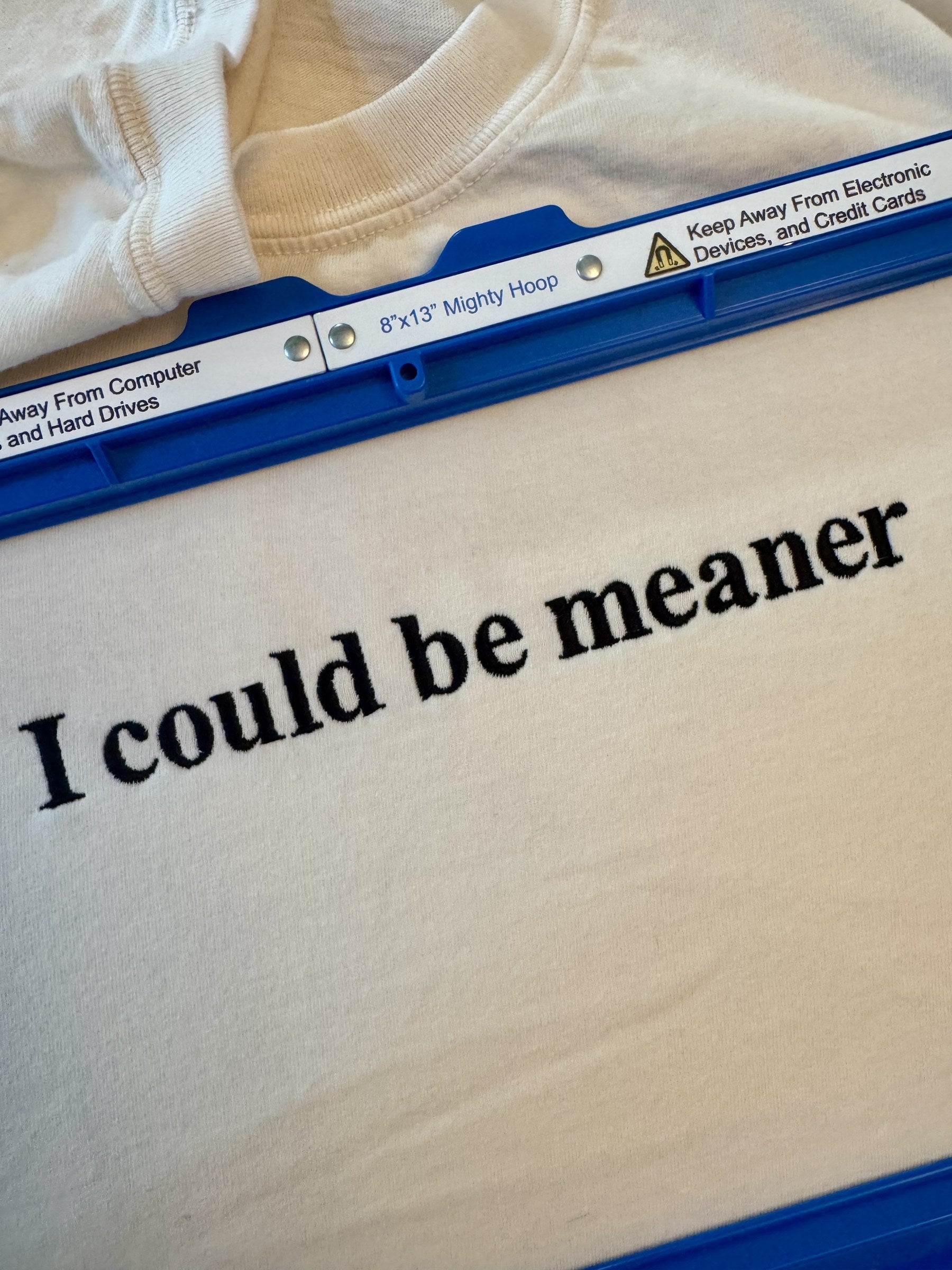 Close-up of the "I could be meaner" embroidery on Ivory, shown in the hoop on the machine