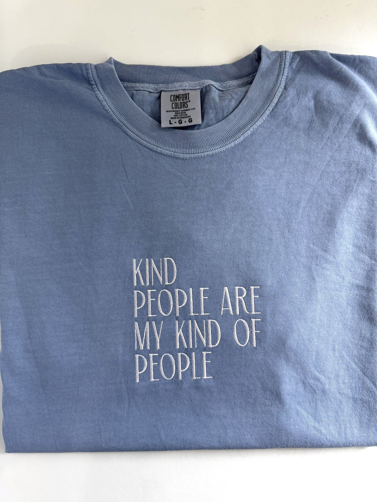 "Kind people are my kind of people" embroidered tee in Blue Jean, folded flat with the collar showing