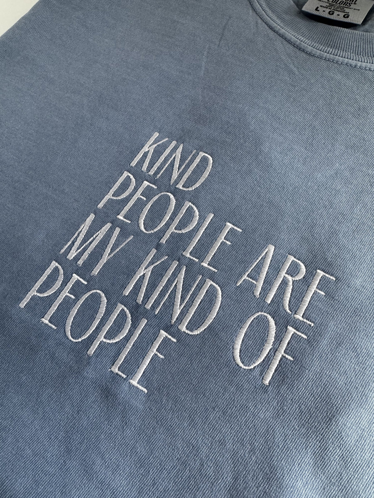 Close-up of the cream embroidered lettering on the "Kind people are my kind of people" tee in Blue Jean