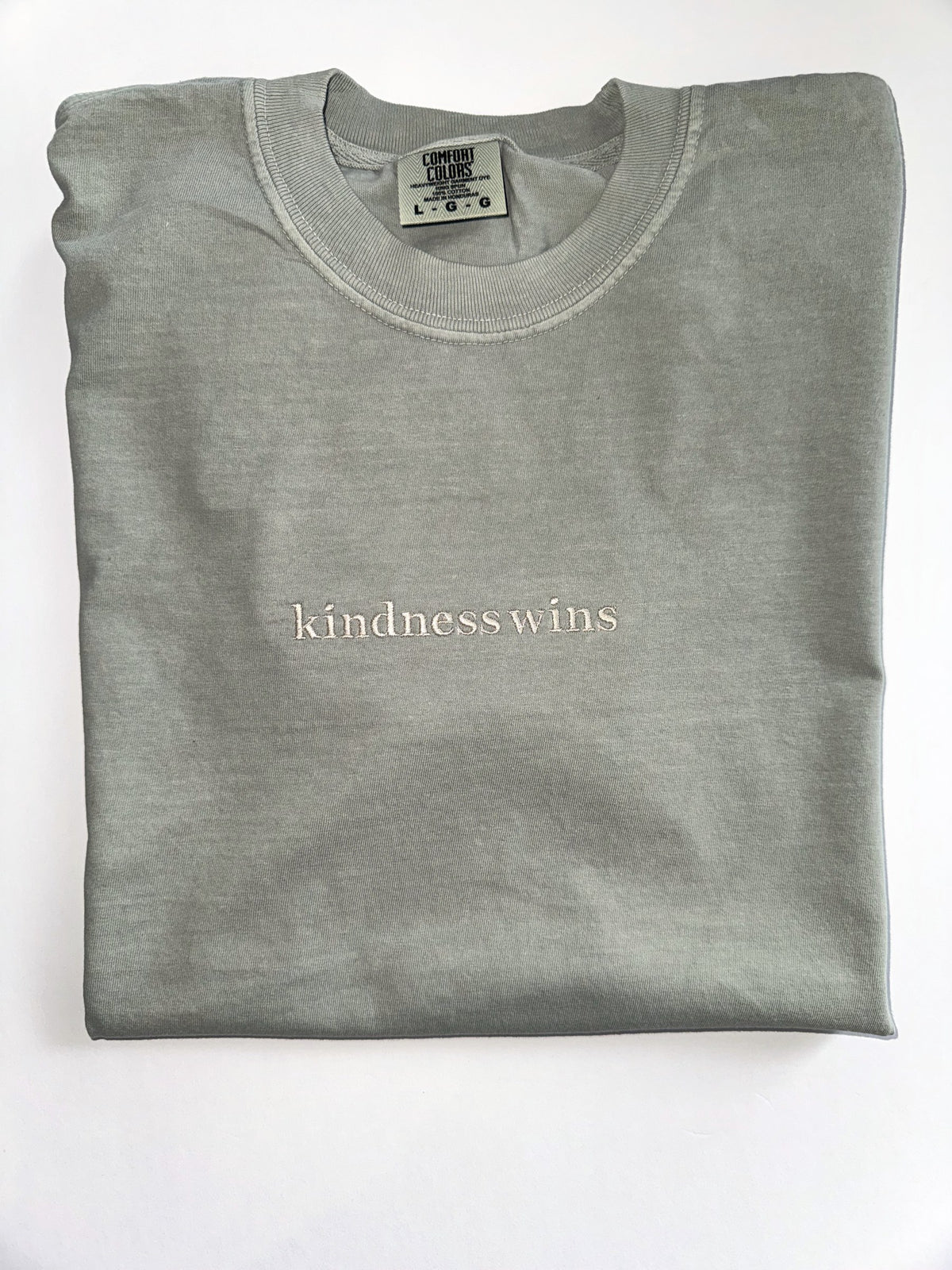 Kindness Wins embroidered in cream thread on a Sage tee
