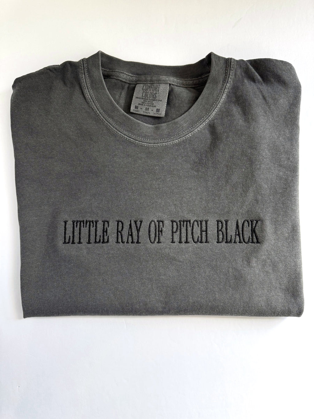 "Little ray of pitch black" embroidered tee in Pepper, folded with the collar showing