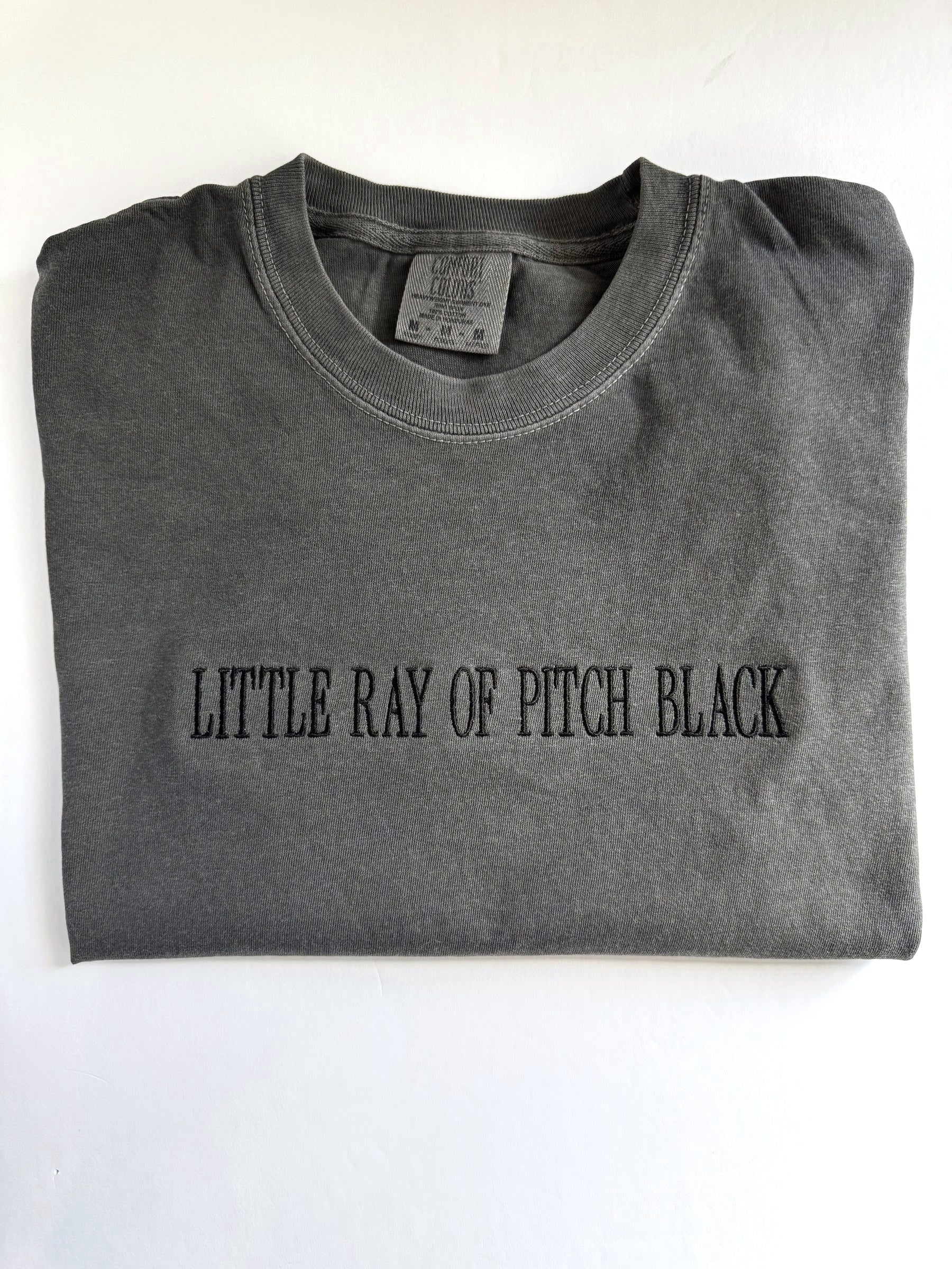 "Little ray of pitch black" embroidered tee in Pepper, folded with the collar showing