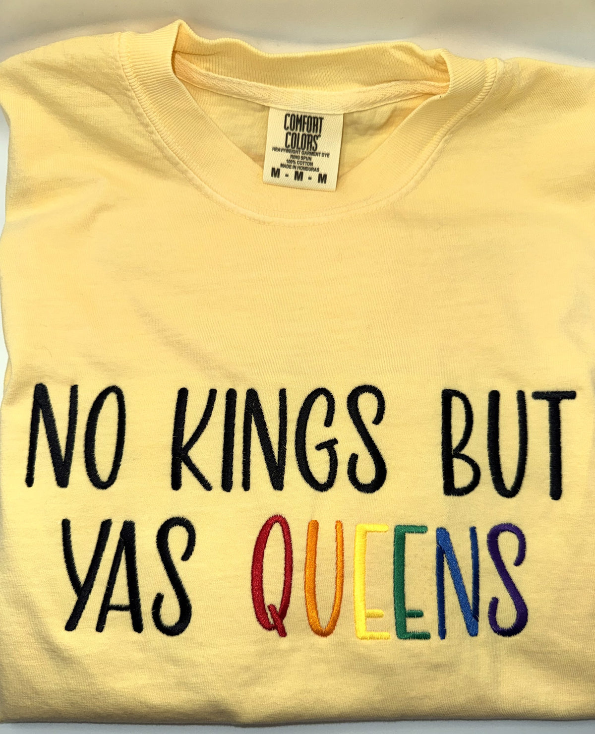 "No kings but yas queens" embroidered tee in Butter, folded flat with the collar showing