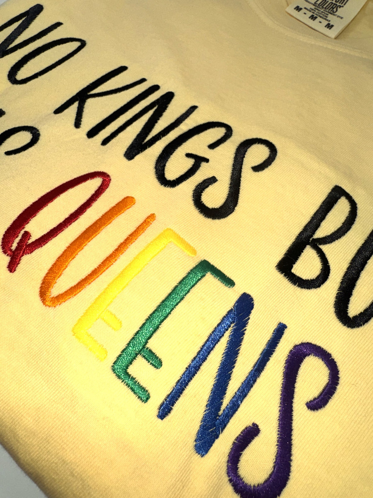 Close-up of the rainbow embroidered QUEENS lettering on the "No kings but yas queens" tee