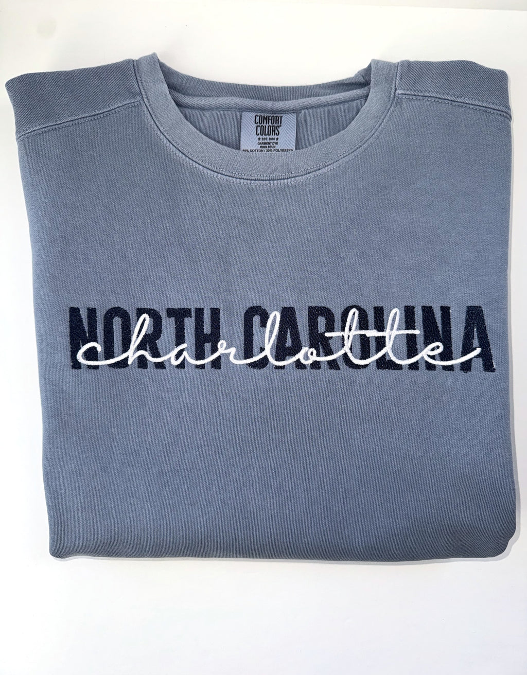North Carolina in navy with Charlotte script in white, embroidered on a Blue Jean crewneck