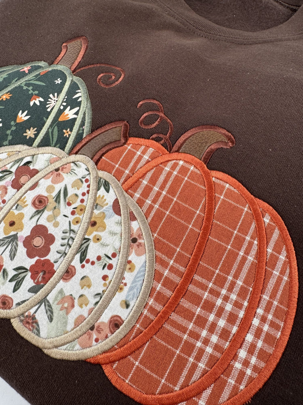 Close up of the orange plaid pumpkin and satin stitched edges on the Dark Chocolate Pumpkin Trio crewneck
