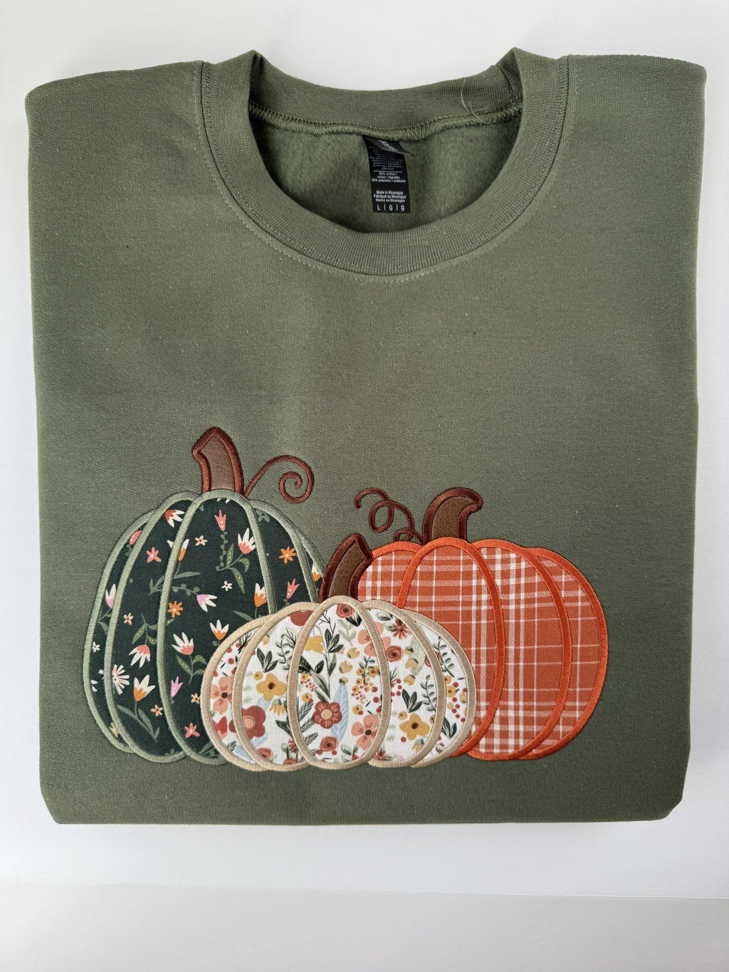 Pumpkin Trio appliqué on a Military Green crewneck: three pumpkins in green floral, cream floral and orange plaid fabric