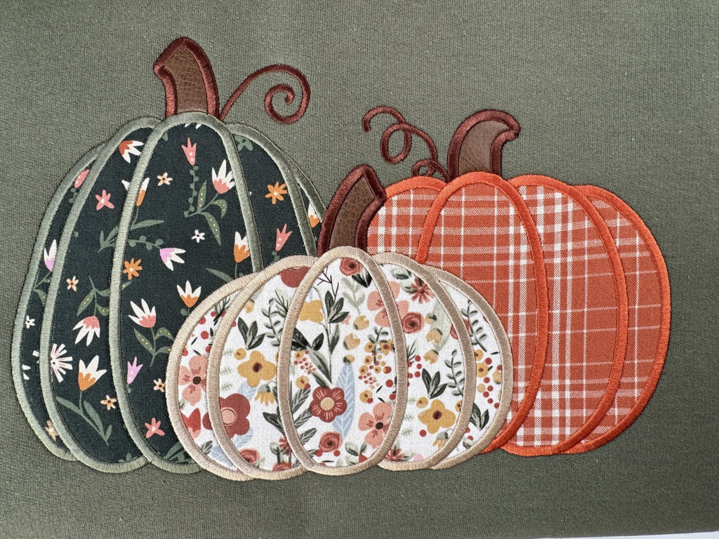 Straight on close up of the three appliquéd pumpkins on the Military Green Pumpkin Trio crewneck