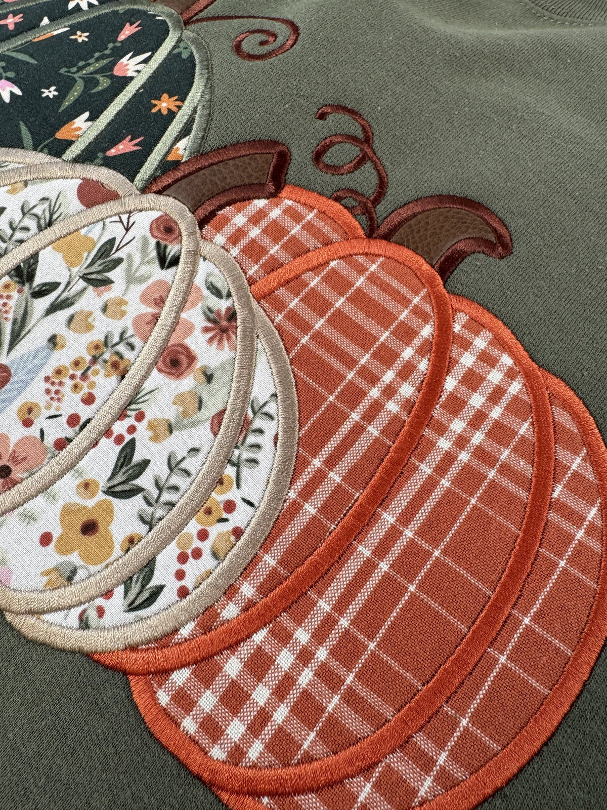 Close up of the orange plaid pumpkin and satin stitched edges on the Military Green Pumpkin Trio crewneck