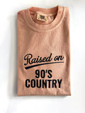 "Raised on 90's Country" embroidered tee in Peachy, folded flat with the collar showing