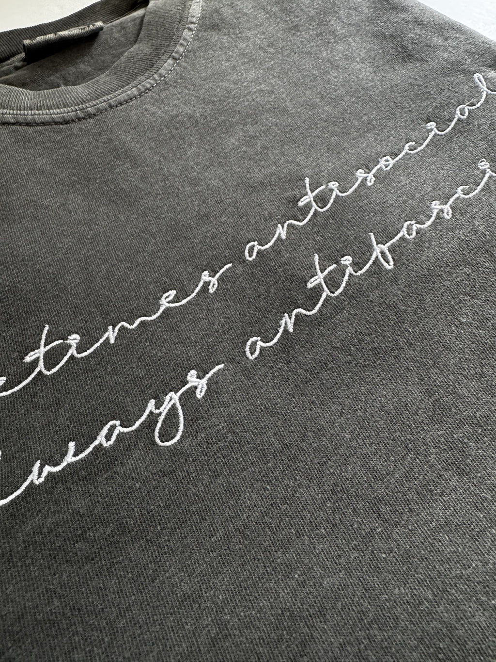 "Sometimes antisocial, always antifascist" script embroidery shown at an angle on a Pepper tee