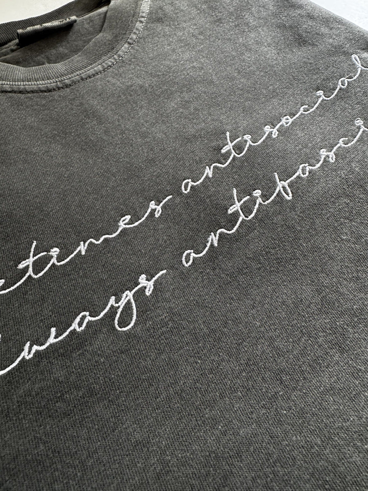 "Sometimes antisocial, always antifascist" script embroidery shown at an angle on a Pepper tee