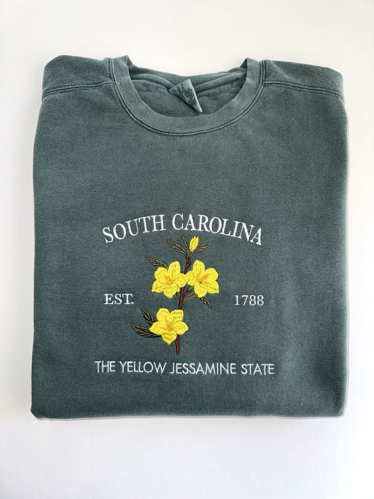 South Carolina Yellow Jessamine embroidery on a folded Blue Spruce crewneck