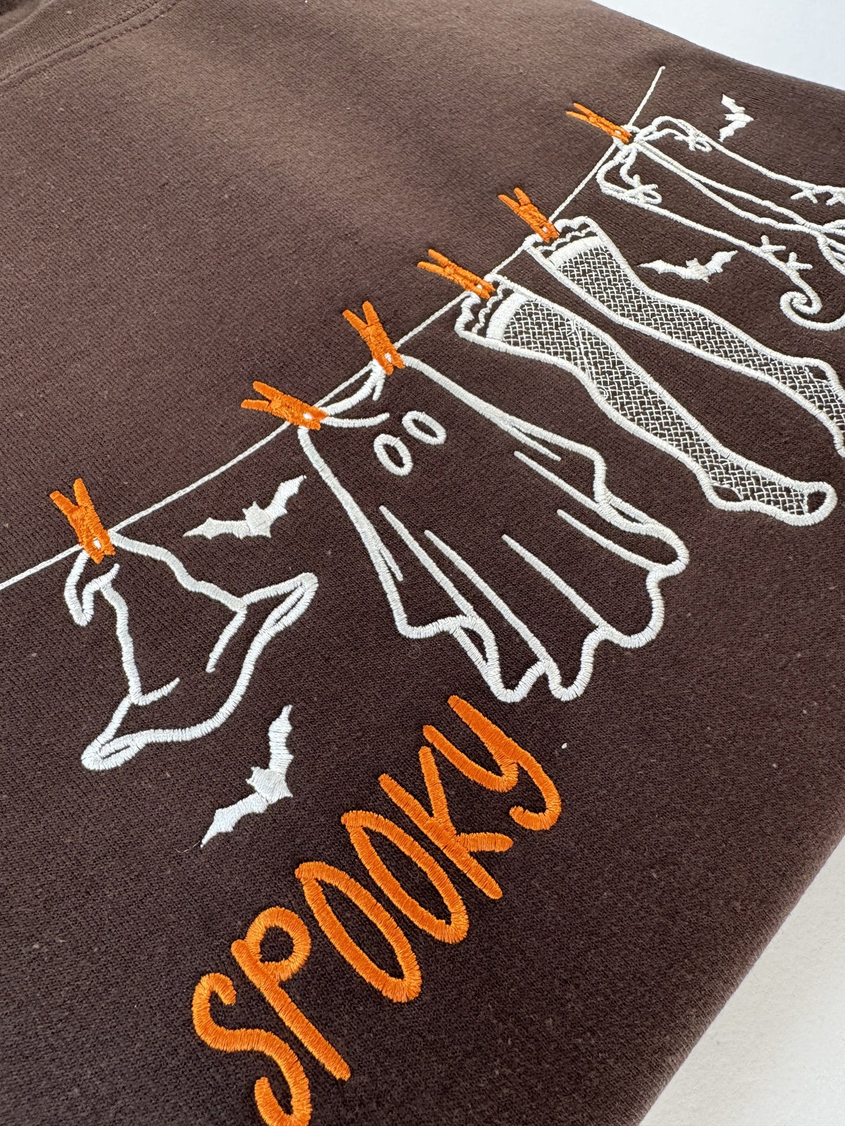 Close up of the witch hat, ghost and orange clothespins on the Dark Chocolate clothesline crewneck
