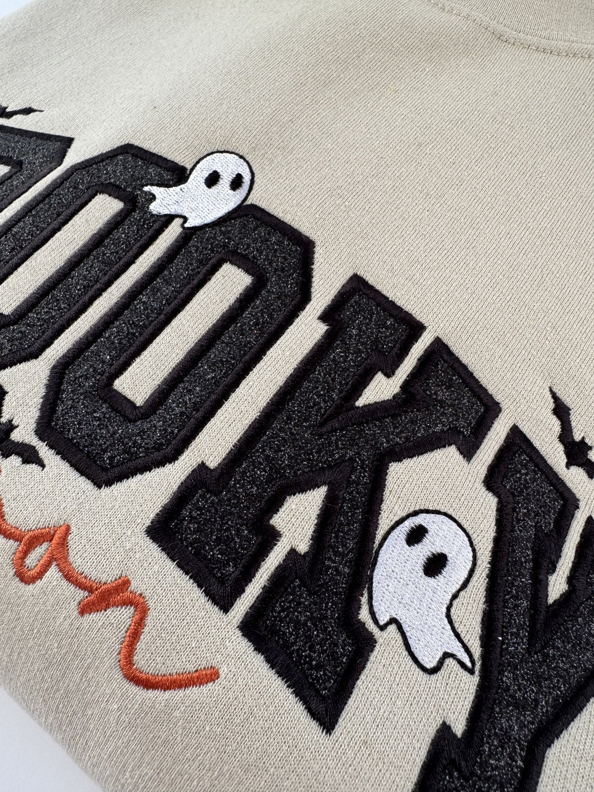 Close up of the black glitter appliqué letters and stitched ghosts on the Sand Spooky Season crewneck