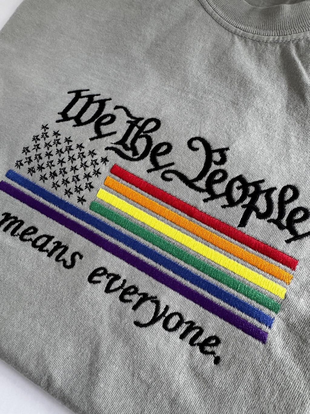 "We The People means everyone" embroidery at an angle, blackletter lettering above a rainbow flag