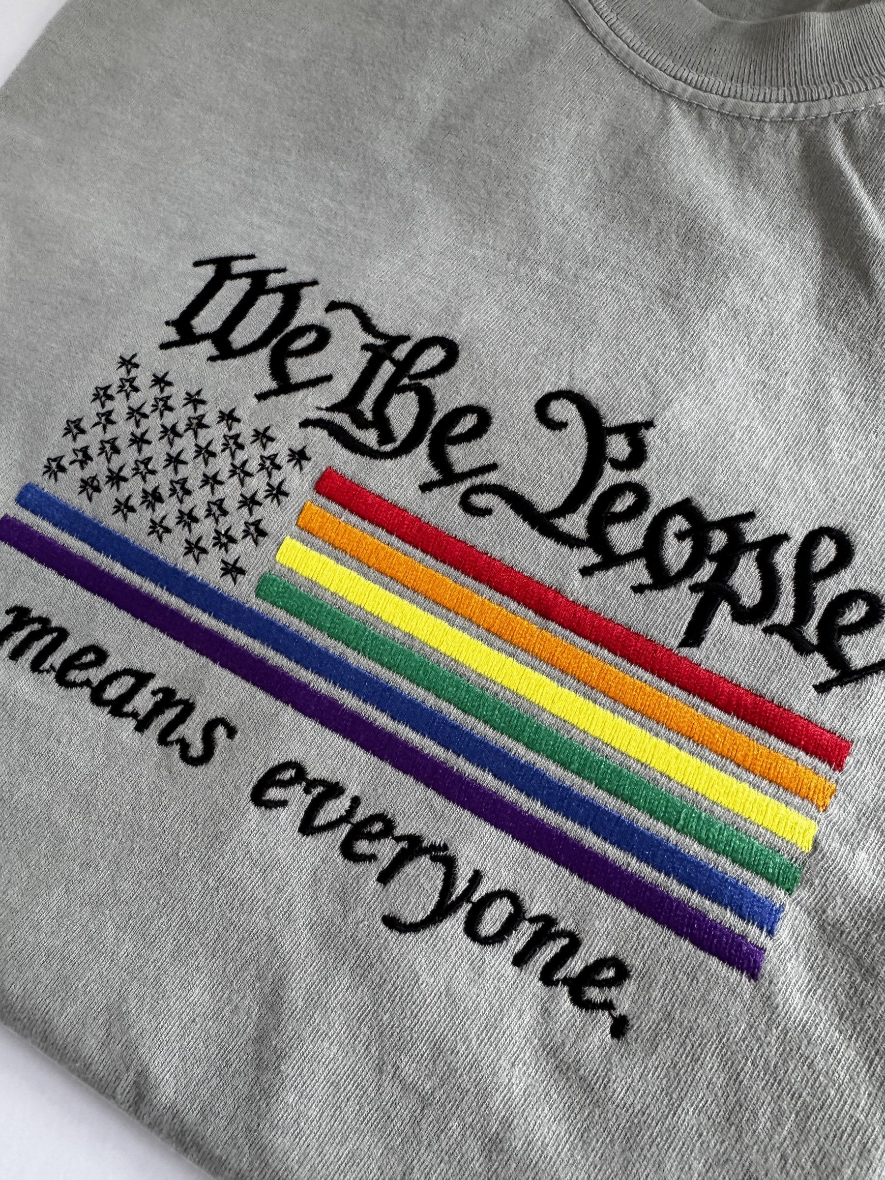 "We The People means everyone" embroidery at an angle, blackletter lettering above a rainbow flag