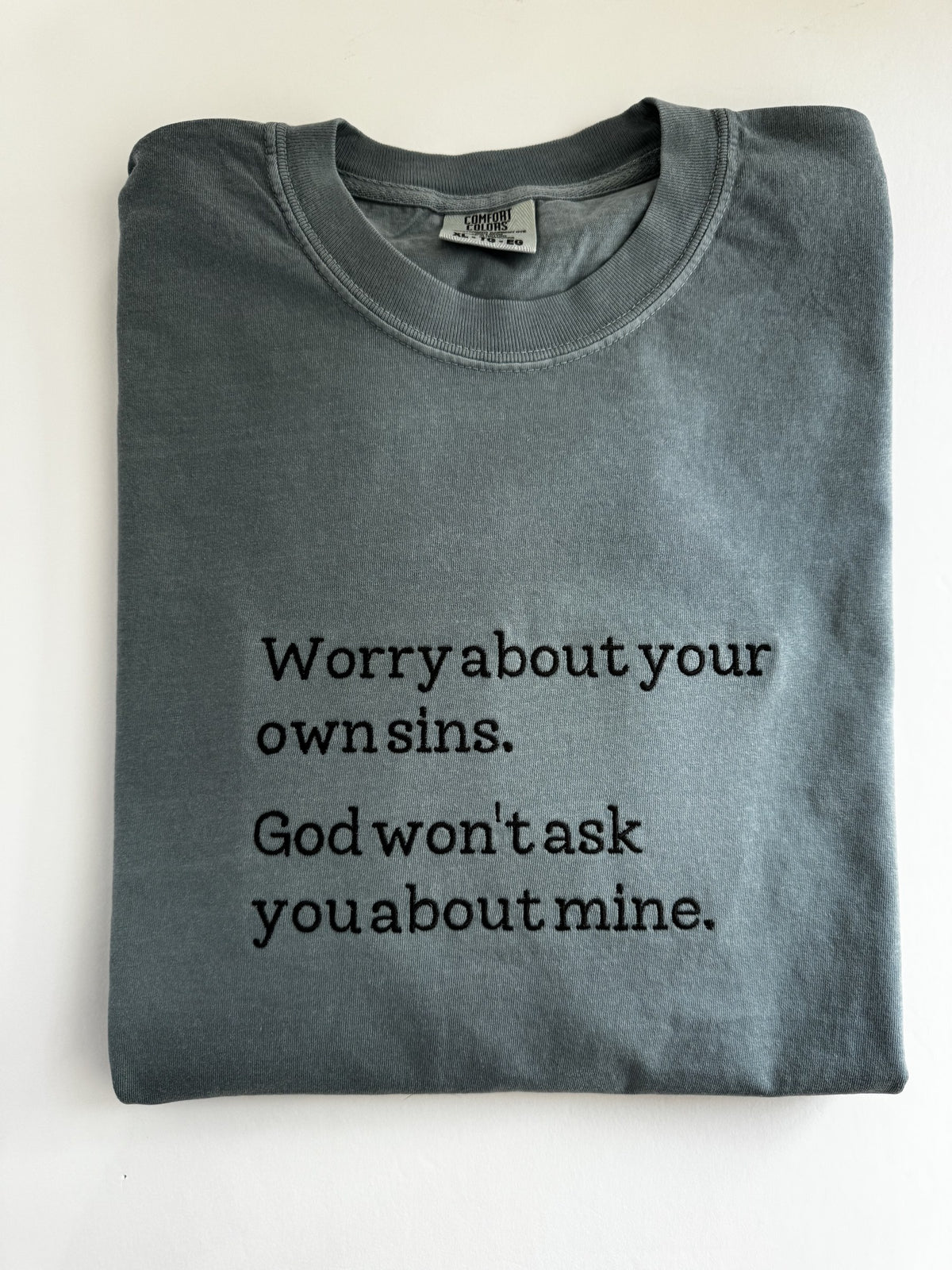 "Worry about your own sins. God won't ask you about mine." embroidered tee, folded flat with the collar showing