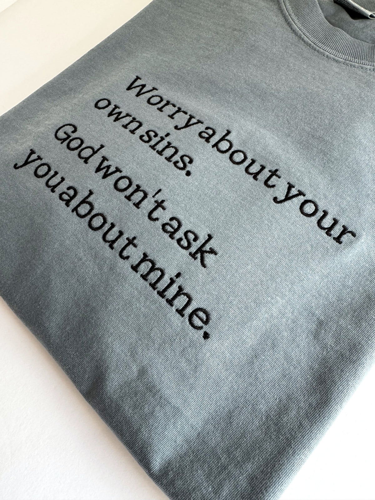 "Worry about your own sins" embroidered tee shown at an angle, dark typewriter lettering