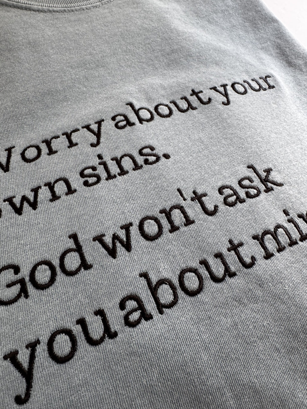 Close-up of the embroidered typewriter lettering on the "Worry about your own sins" tee