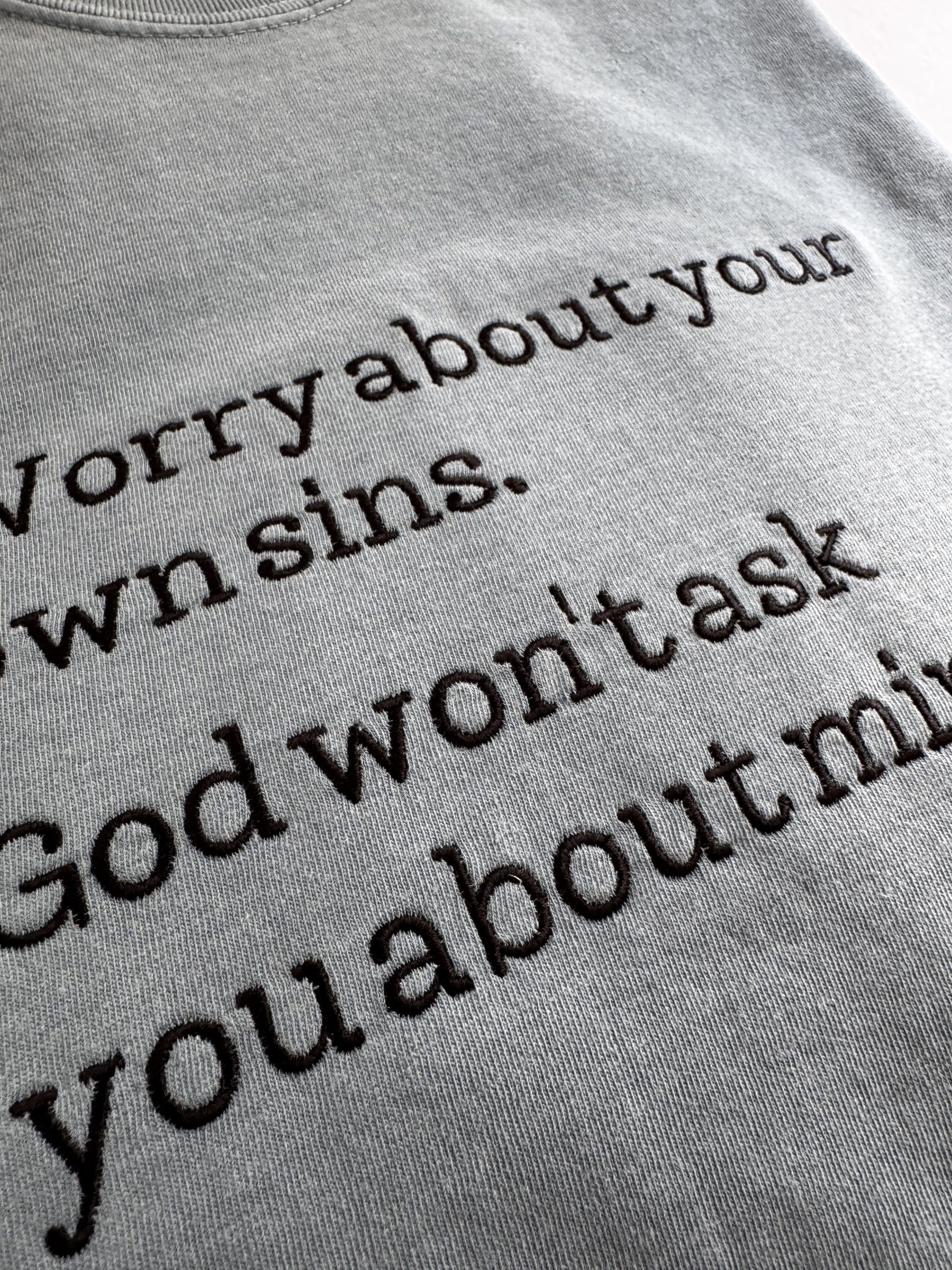 Close-up of the embroidered typewriter lettering on the "Worry about your own sins" tee
